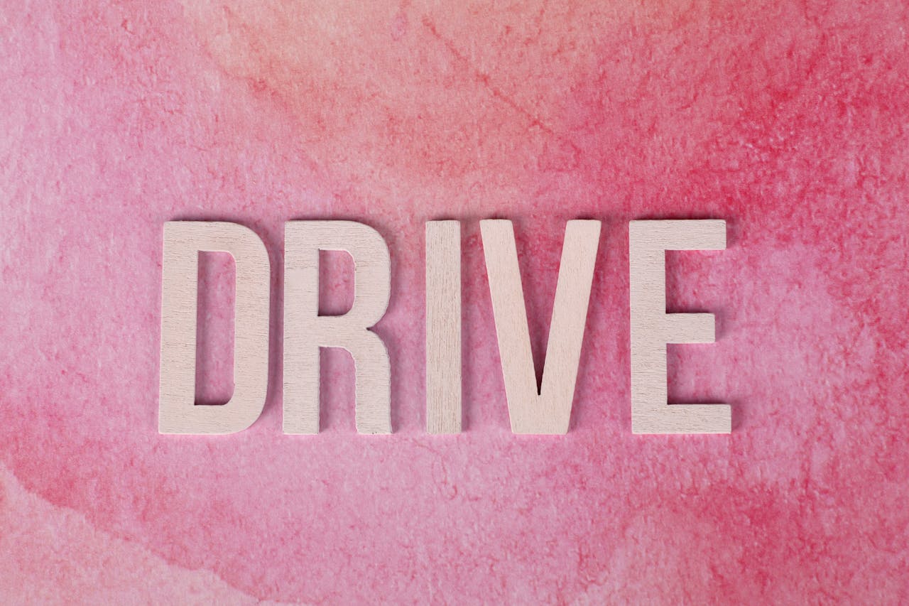Wooden letters spelling Drive on a textured pink background, inspiring motivation and action.
